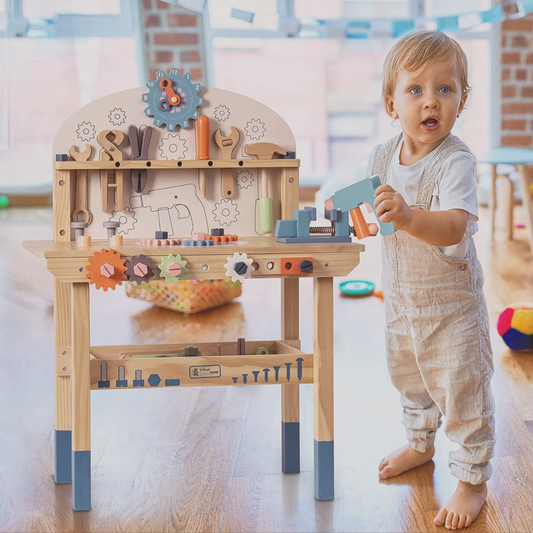 Child playing with a wooden toy workbench in a room with toys scattered around.